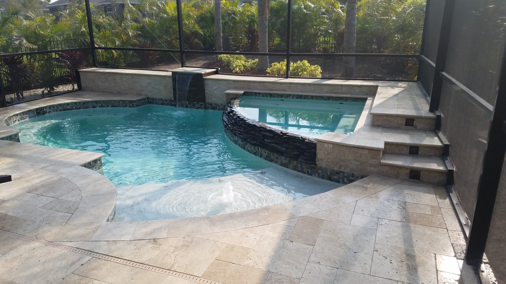 Freeform pool with raised spa, stacked-stone spillway wall and sheer-descent waterfall — Apollo Travertine Spa Retreat, an Apollo Beach, FL pool project by Wahoo Pools