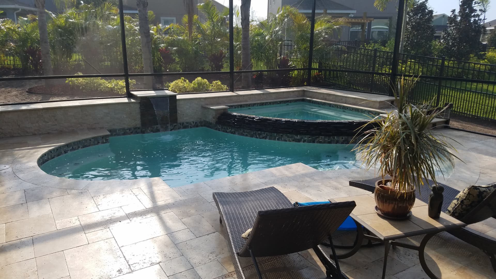 Screen-enclosed pool and spa with glass waterline tile and travertine deck seen from the lanai — Apollo Travertine Spa Retreat, an Apollo Beach, FL pool project by Wahoo Pools