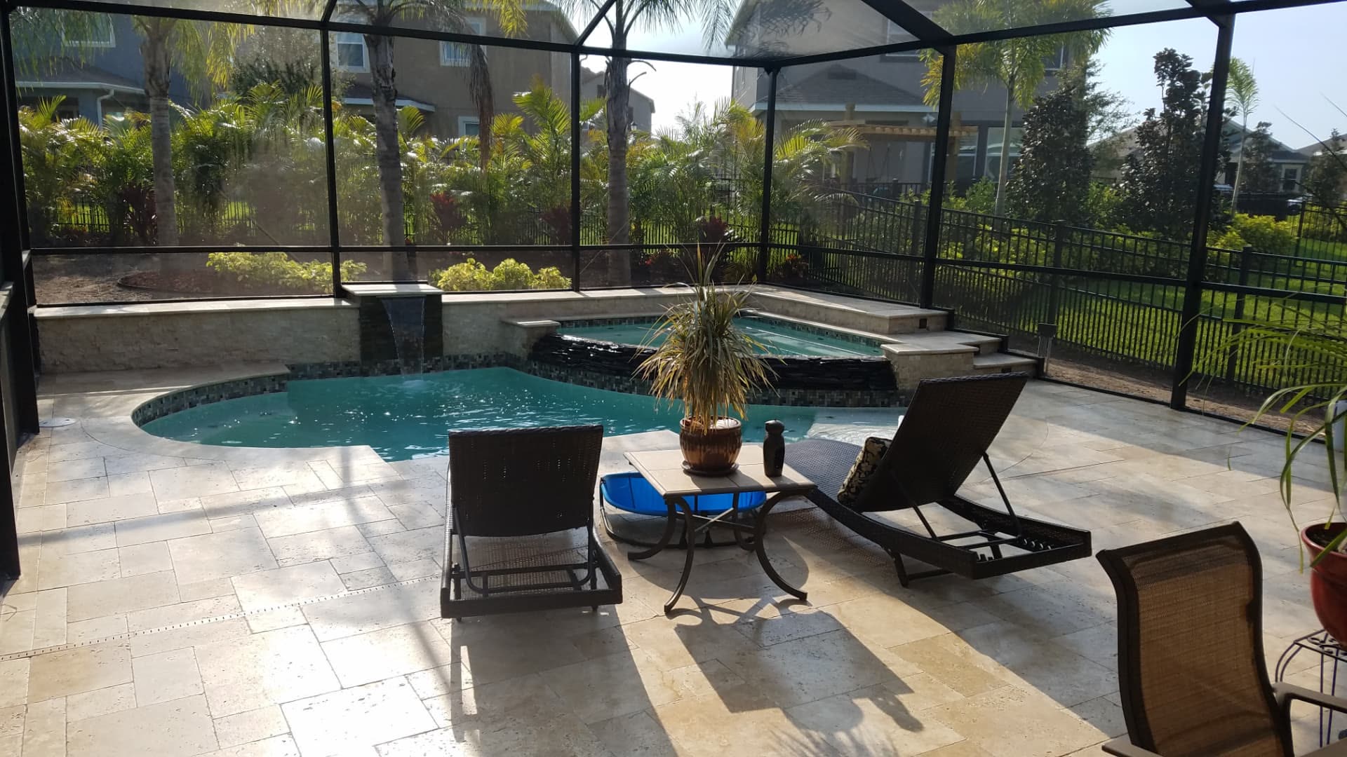 Travertine pool deck with loungers and tropical landscaping inside the screen enclosure — Apollo Travertine Spa Retreat, an Apollo Beach, FL pool project by Wahoo Pools